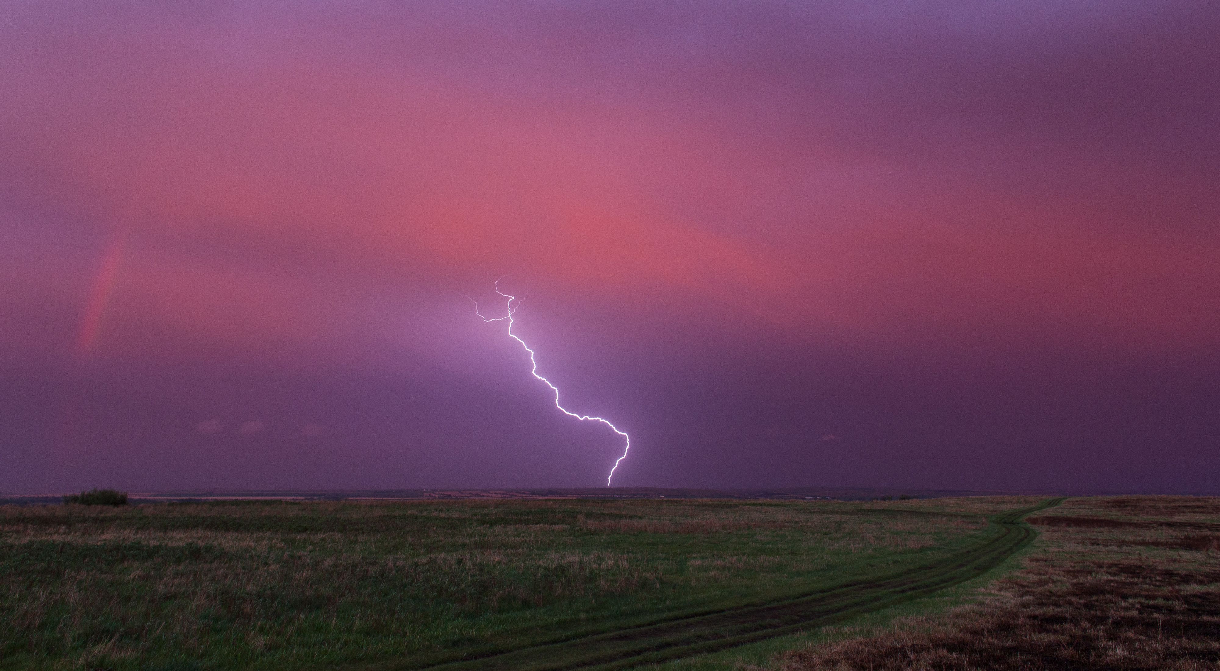 Lightning strikes the prairie out of a pink-purple sky.