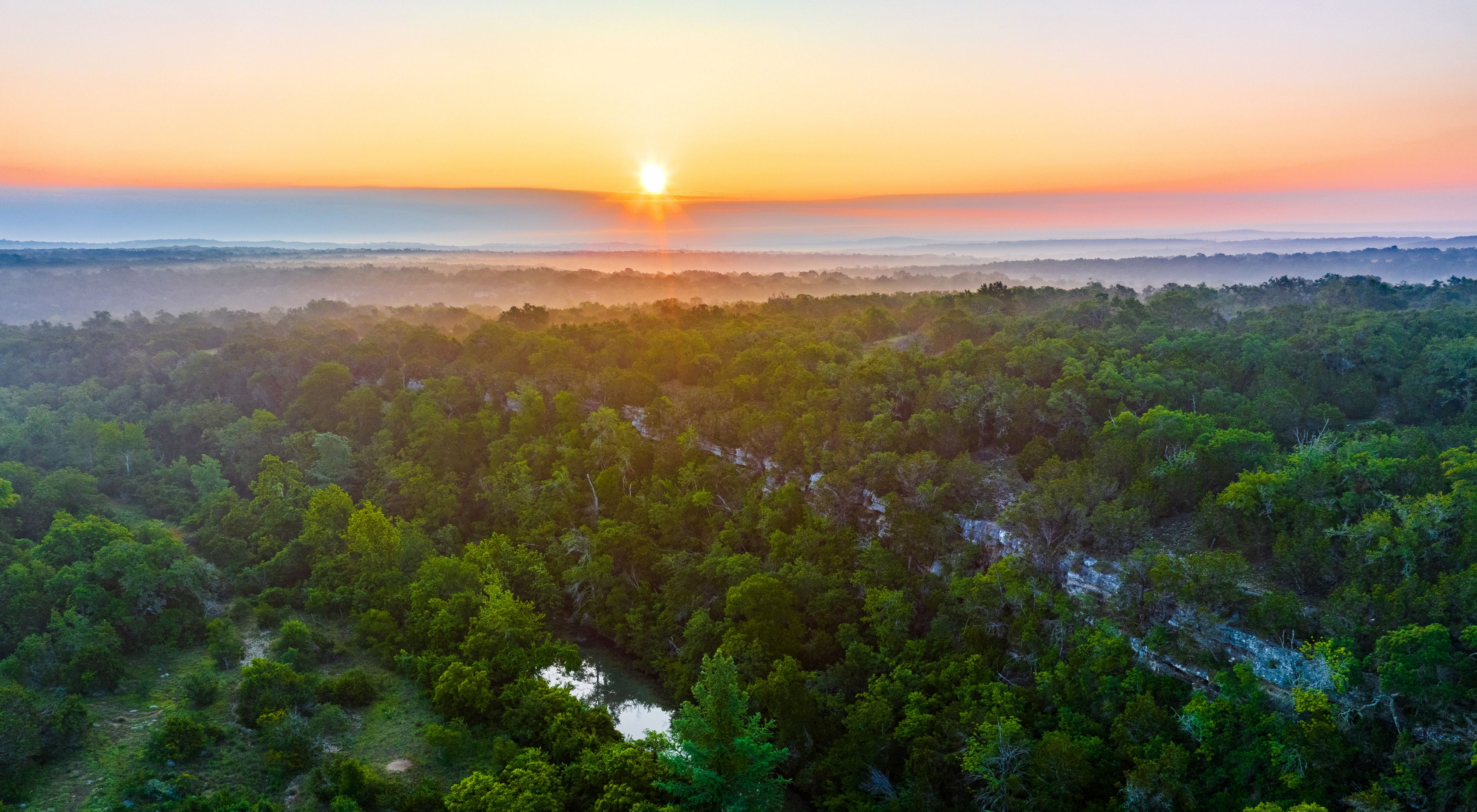 The sun rises over a vast expanse of green brush and a blue river.
