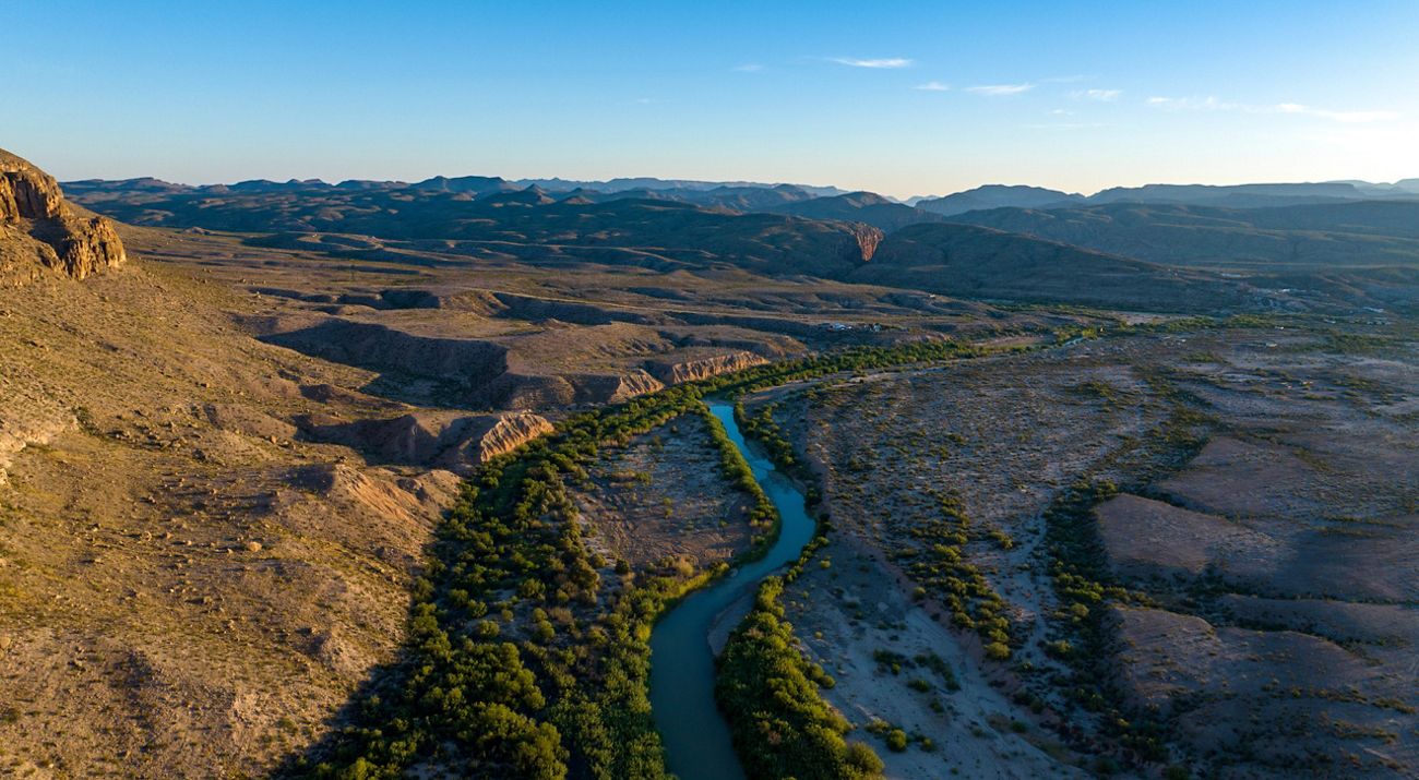 A winding blue river lined with brush lies next to sweeping cliffs and canyons.