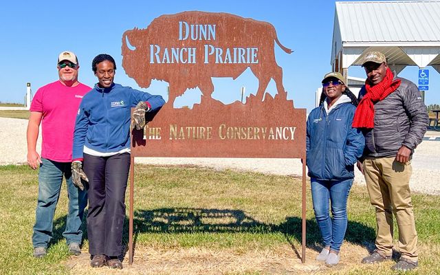 Four people stand by a sign that says Dunn Ranch Prairie.