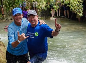 Two white men posing in front of water.