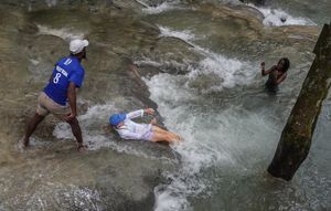 A woman slides on a rocky falls into water.