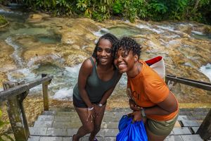 Two jamaican women pose in front of water.