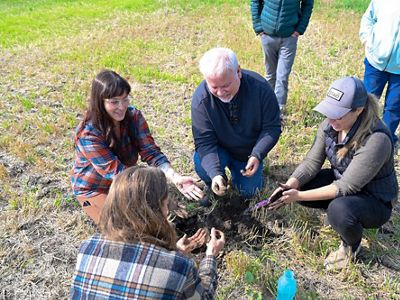 A group of people kneeling in a circle touching soil.