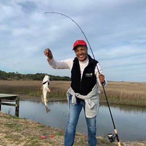 Dale Threatt-Taylor sostiene una caña de pescar en una mano y de su otra mano cuelga un pez capturado.