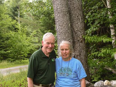 A man and woman standing in front of woods.