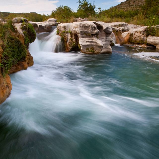 Turquoise water tumbles over large boulders creating a waterfall on a rocky, flowing river.