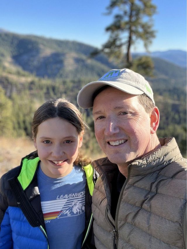 A man and girl pose together in front of a rolling mountain ridge.