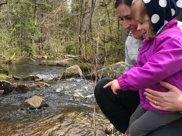Eileen Bader Hall and her daughter watch as alewives migrate in a newly restored stream in Maine.