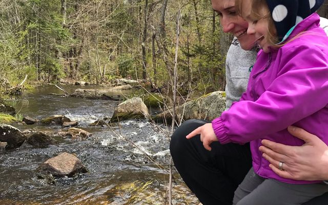 Eileen Bader Hall holds her daughter while they look into a flowing stream.