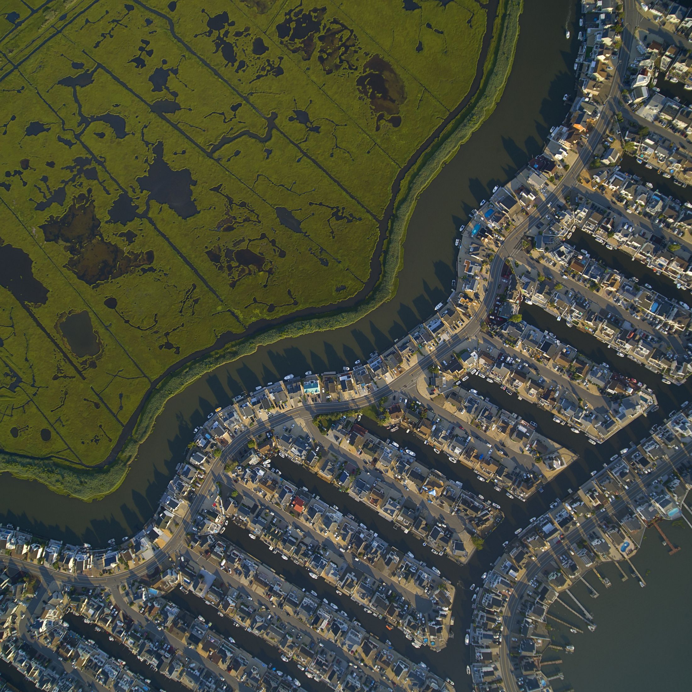 Canal seen from above: On one side dozens of houses sit right against the water, on the other green marsh grasses grow