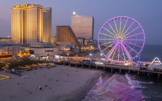 buildings with many lights, including a Hard Rock casino/restaurant and a purple lit up ferris wheel are seen on the edge of the beach and on a dock stretching into the ocean