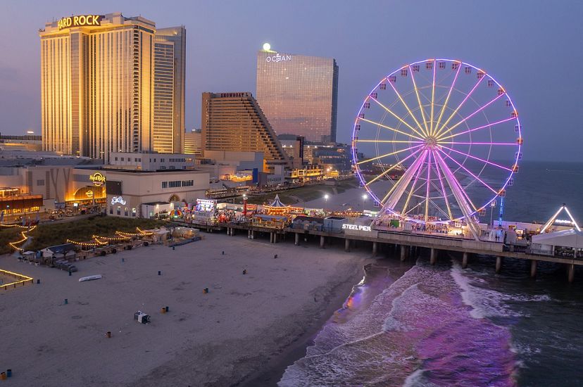 buildings with many lights, including a Hard Rock casino/restaurant and a purple lit up ferris wheel are seen on the edge of the beach and on a dock stretching into the ocean