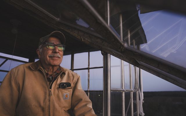 Man in tan jacket stands in fire tower at twilight. 