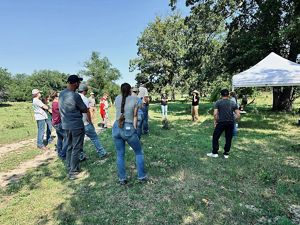 A group of people gathered around listening to someone speak in a field.