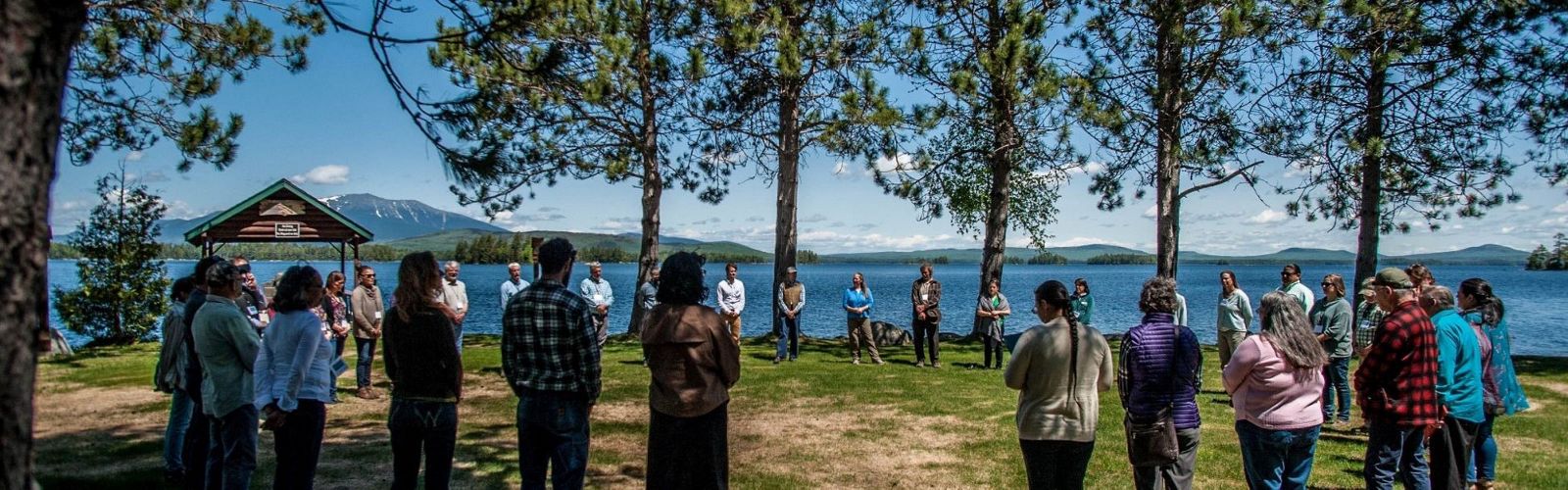People stand in a circle with a lake behind them.