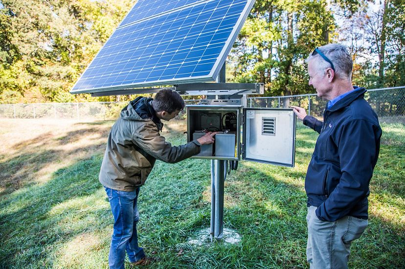 Two men stand next to a small solar panel that powers a suburban smart storm pond. 