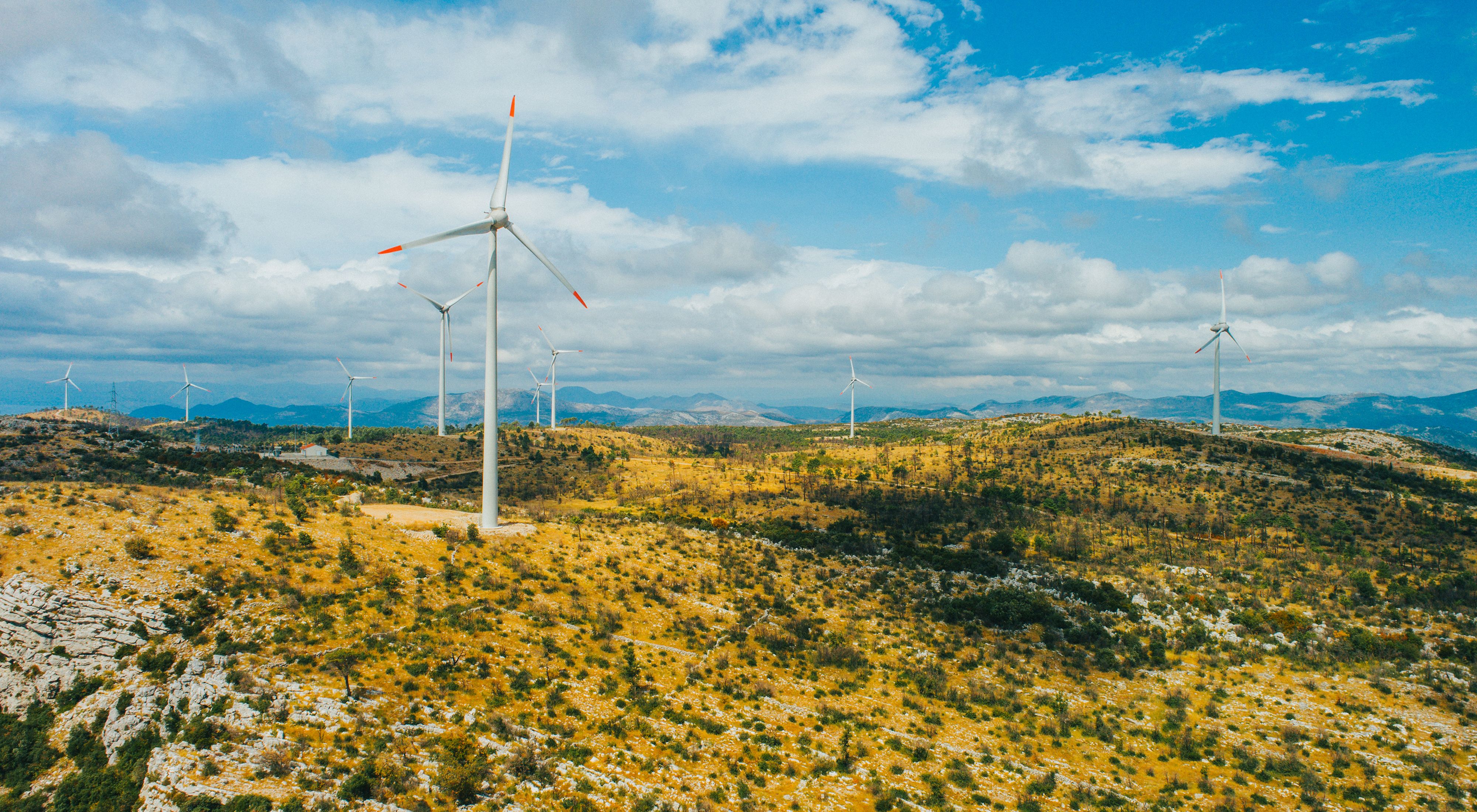 Scenic mountainous landscape with wind turbines against cloudy sky.