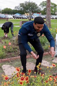A man sprinkles seeds in a park while a woman behind him plants flowers.