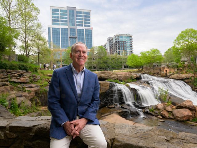 Greenville Mayor Knox white sits on a rock in a riverfront park.