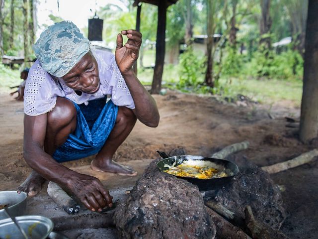 Woman crouches next to cooking fish