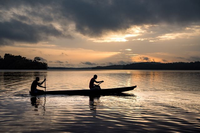 Photo of two people paddling a canoe on a river in Gabon.