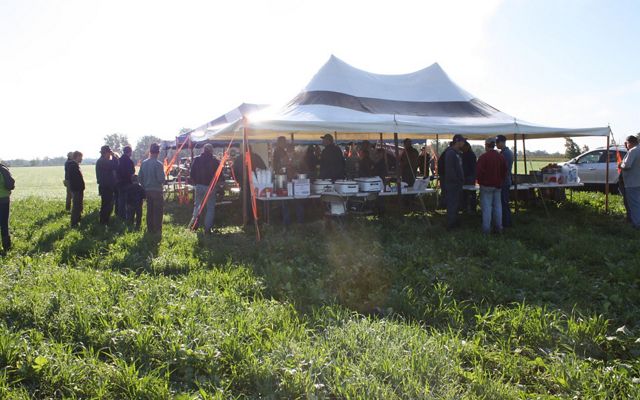 A group of farmers gather under a large tent in a field for a meeting on a sunny day in Michigan's Saginaw Valley. 