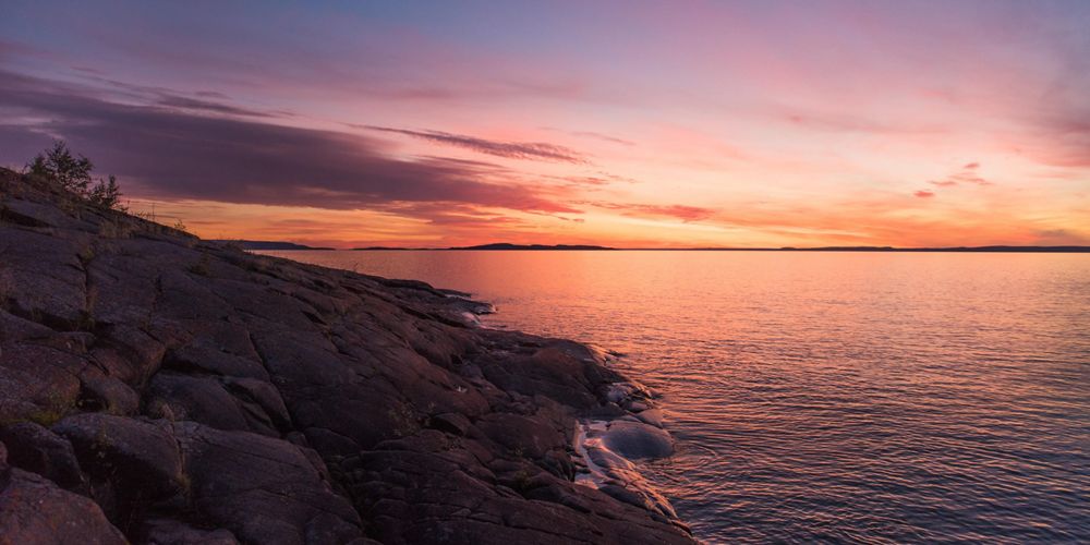 View of rocky coast next to a lake with a colorful sunset in the background