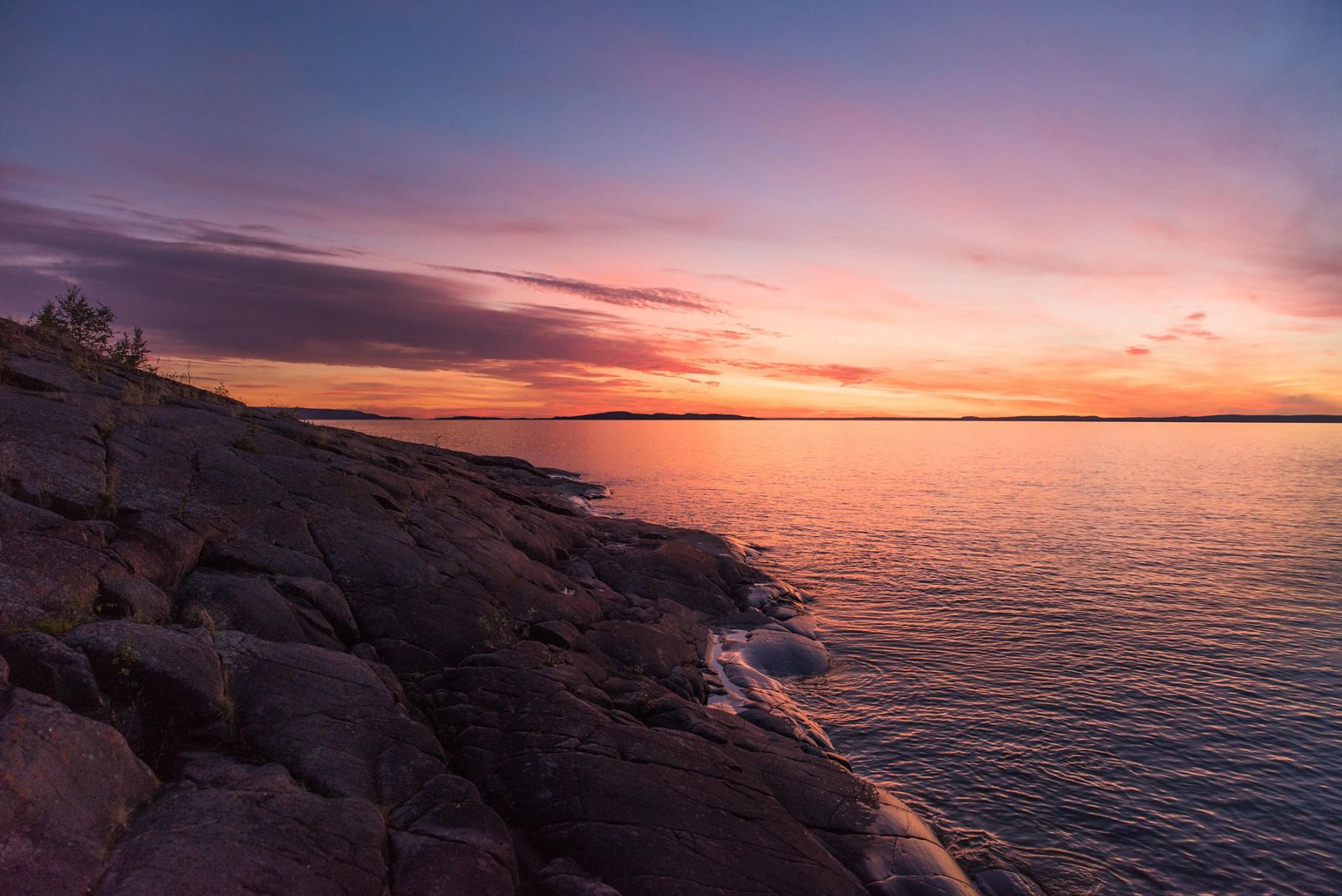View of rocky coast next to a lake with a colorful sunset in the background