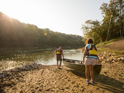 Two people put their canoe in the water on the Green River's muddy banks.