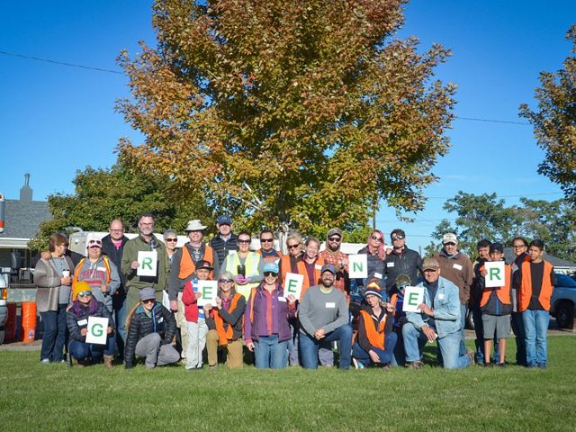 A large group of volunteers poses for a photo holding letters that spell out the word "greener."