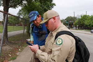 Two men stand together looking at a cell phone.