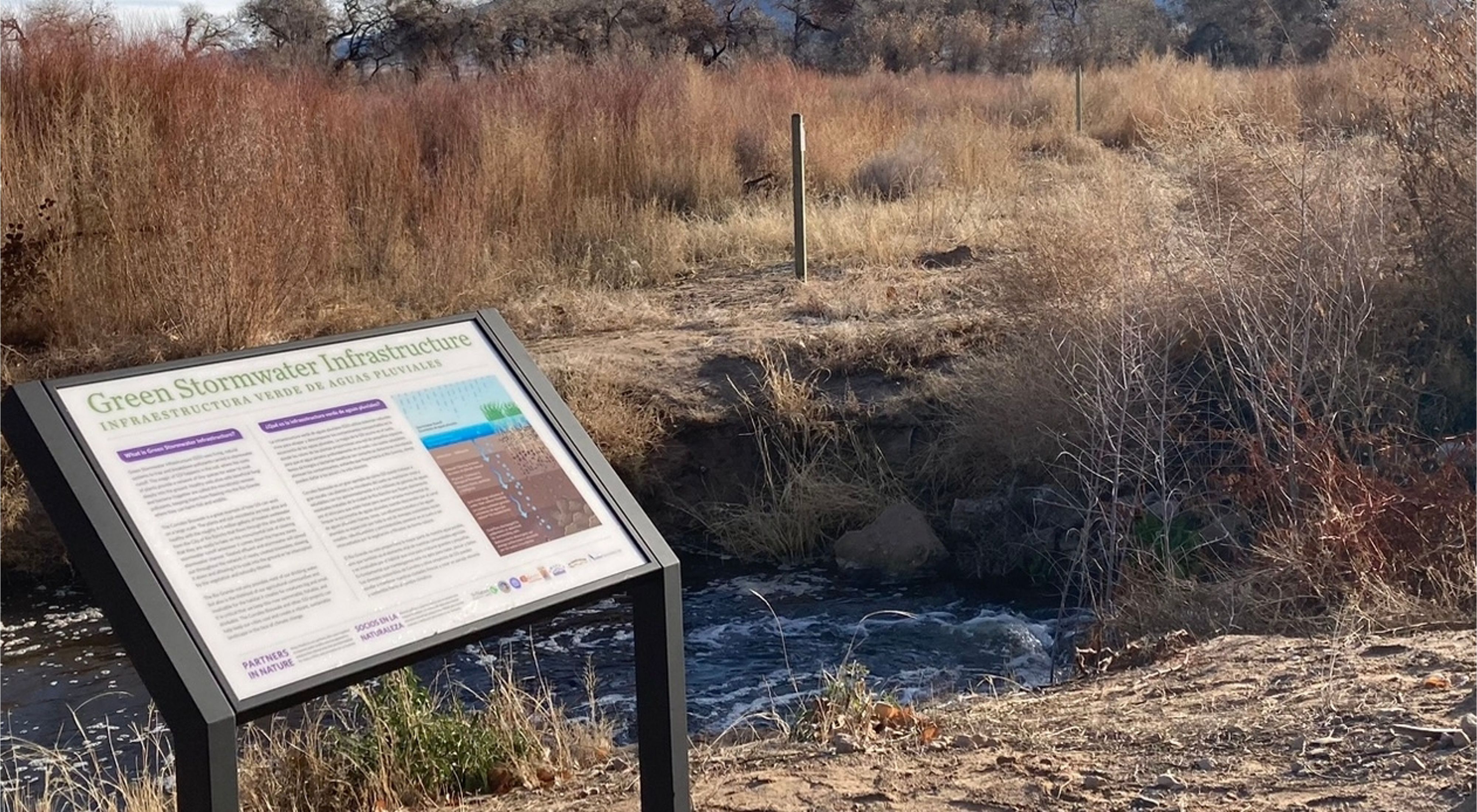 Closeup of an interpretive sign amid a scrubby landscape; the sign describes green stormwater infrastructure.