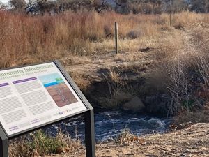 Closeup of an interpretive sign amid a scrubby landscape; the sign describes green stormwater infrastructure.