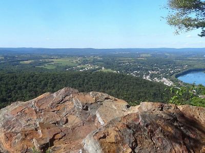 View of the Susquehanna River valley seen from a rocky outcrop. A bend in the river is visible to the right. Green forests and open fields stretch out to the horizon.