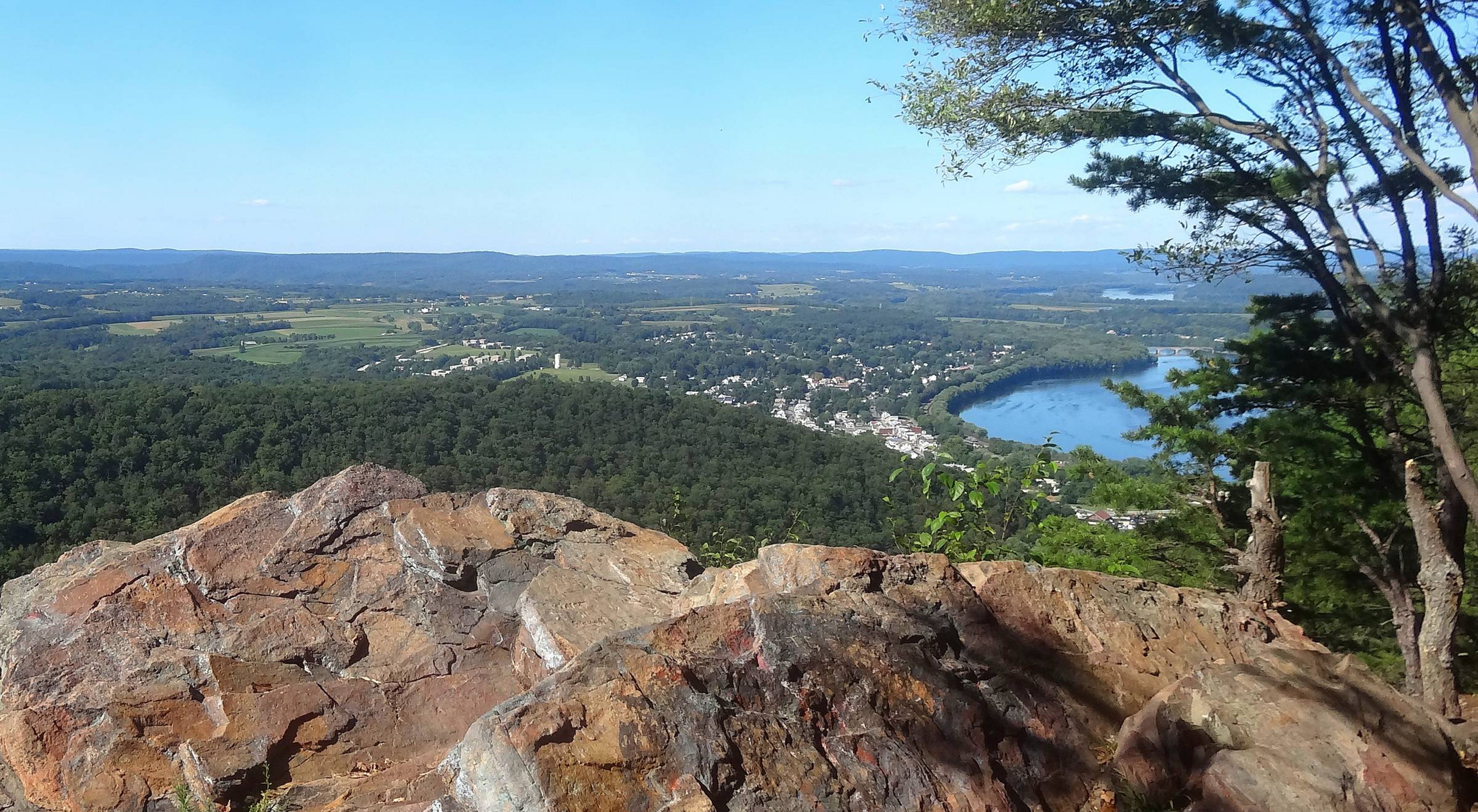 A view of a lookout over a large rock over looking a forested area and small river.