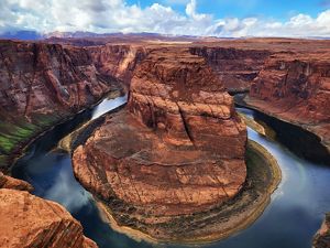 A wide river makes a horseshoe shape, wrapping around a large orange rock in a canyon.