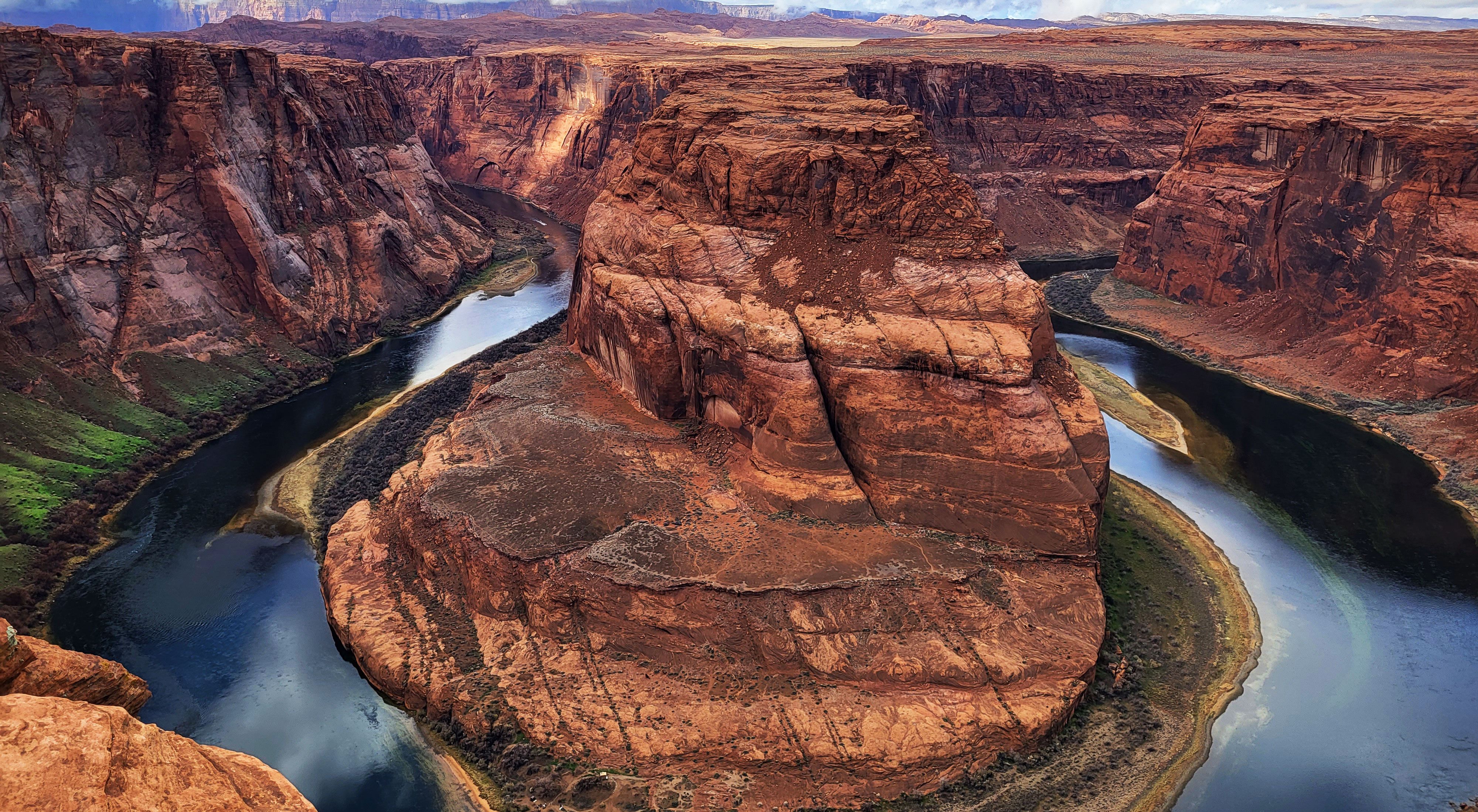 A wide river makes a horseshoe shape, wrapping around a large orange rock in a canyon.