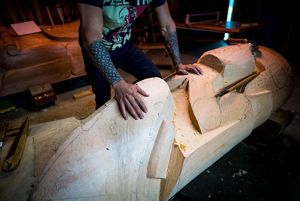People inside a shed laying their hands on a newly constructed totem pole.