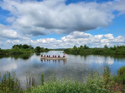 A group of people in a ten-person canoe on the water as seen from the bank at Emiquon.