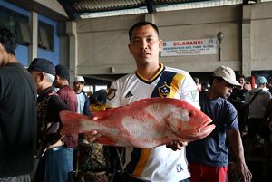 A man holds a large red fish in a busy market. 