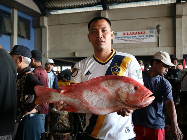 A man holds a large red fish in a busy market. 