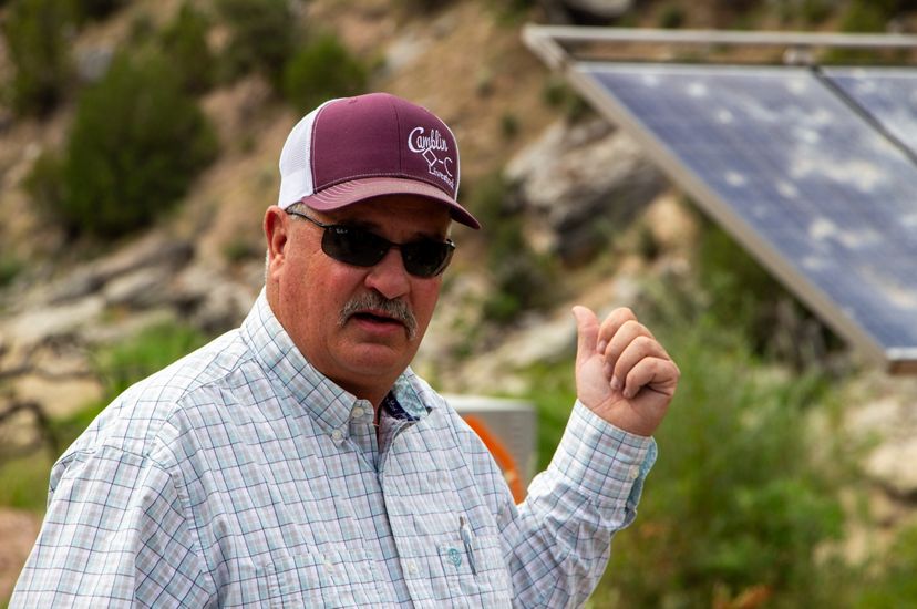 A man gestures to a solar panel behind him.