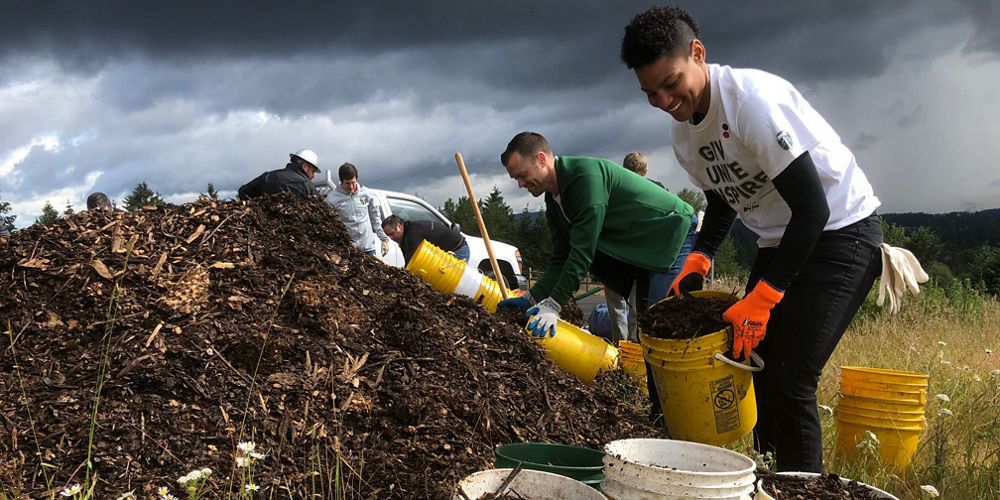 Several volunteers with work gloves and buckets by a pile of dirt with a white pick up truck.