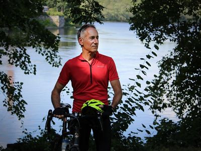 Josh Royte stands next to his bike with a river in the background.