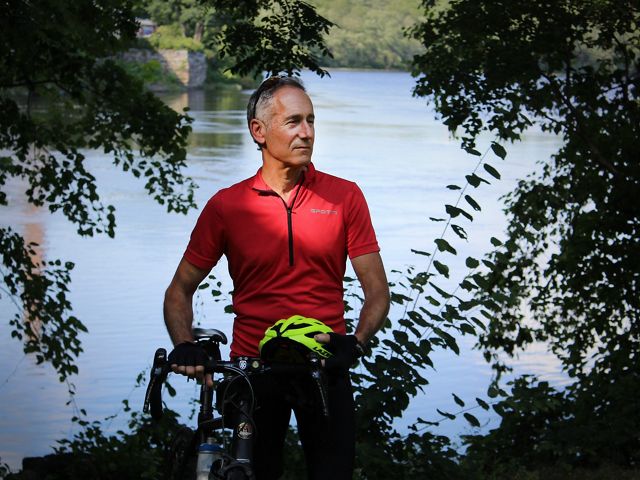 Josh Royte stands next to his bike with a river in the background.