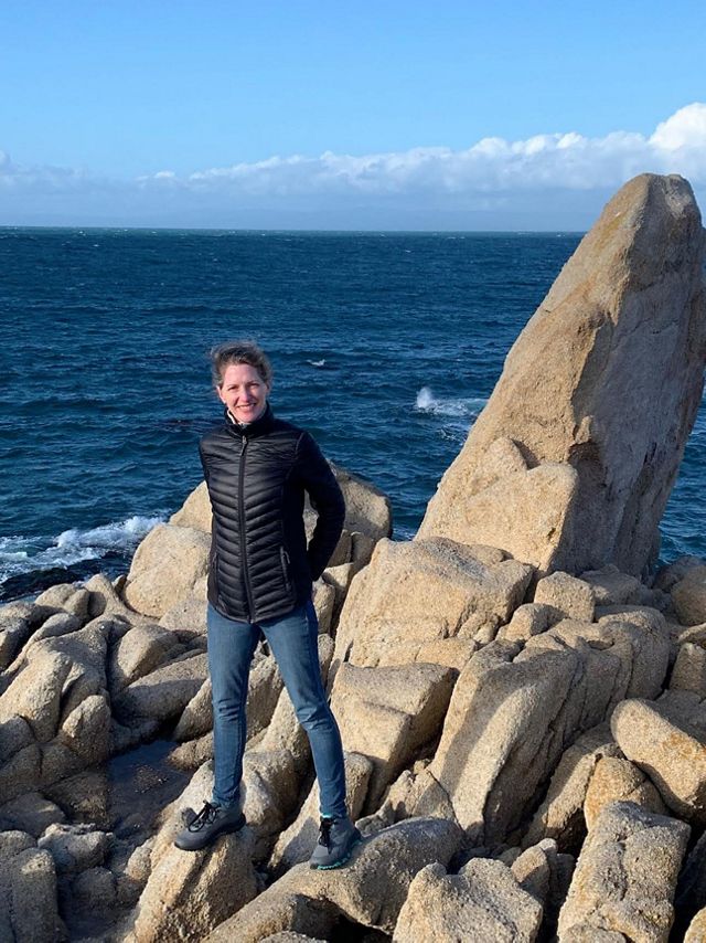 kathleen standing on rocks with the ocean behind her.