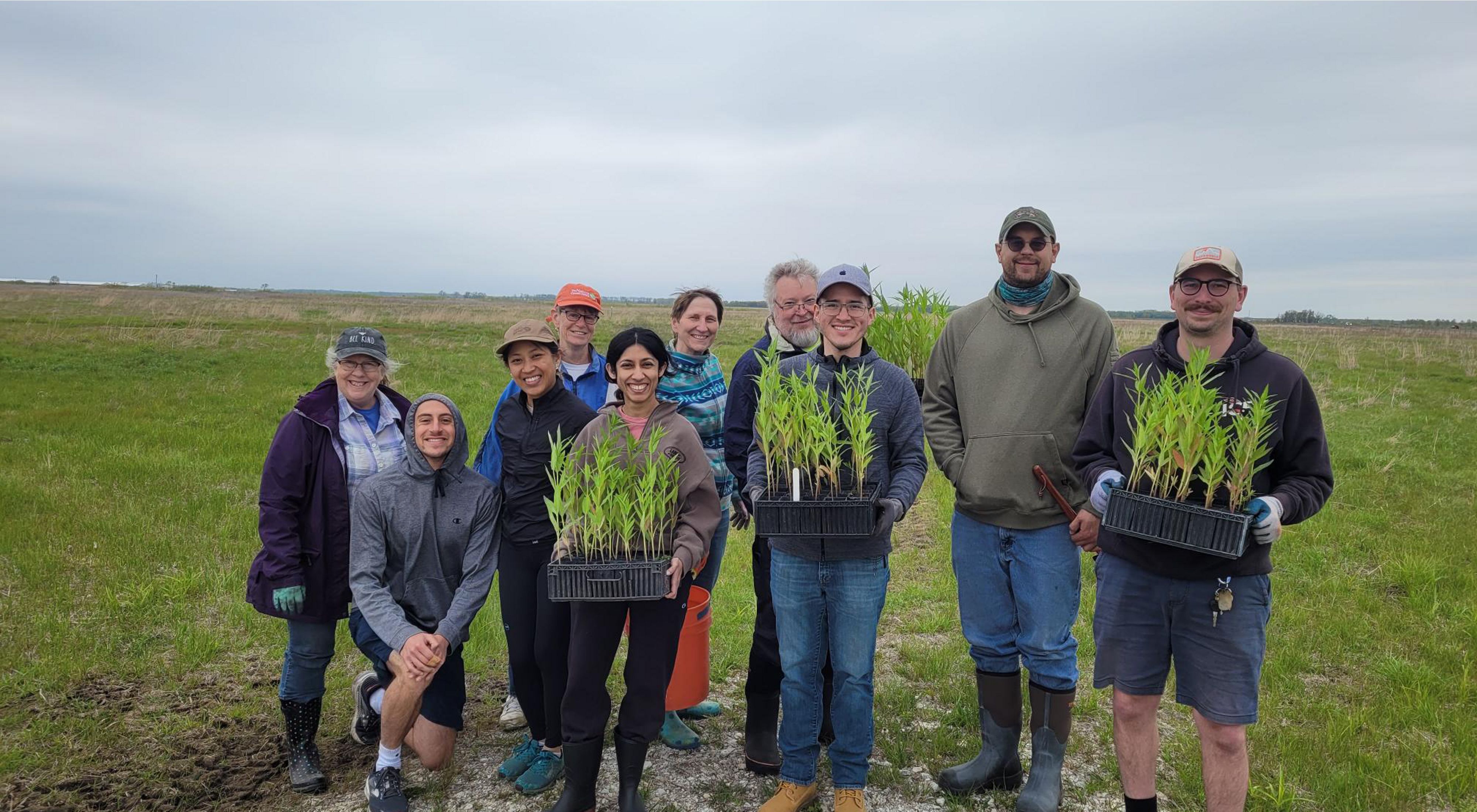 A group of volunteers holding flat containers of small plants pose together on the Kankakee Sands prairie.