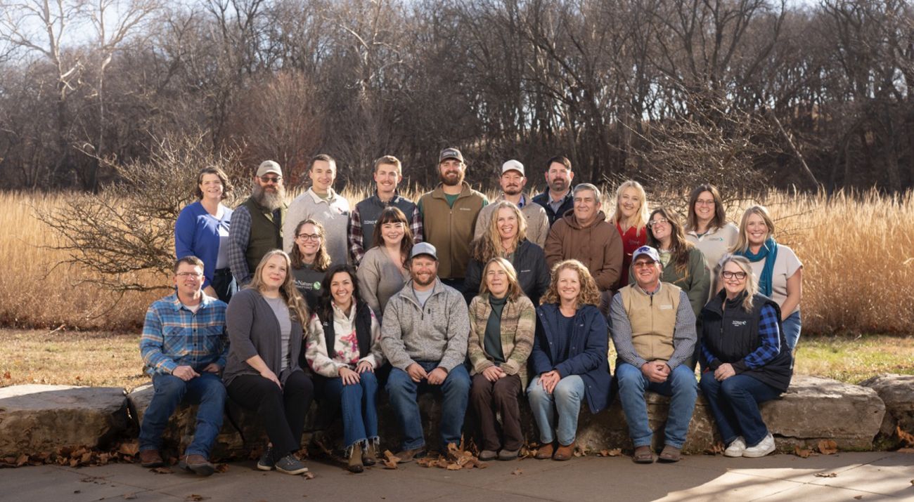 Group photo of about 20 staff members sitting and standing outside with forest in the background.