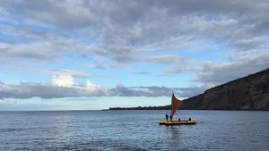 A bay in Hawai'i with two boats headed back in to shore with a green mountain rising in the background.